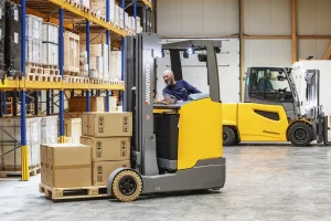 Zu sehen sind zwei Gabelstapel die geschäftig in eine Lagerhalle Ware transportieren.