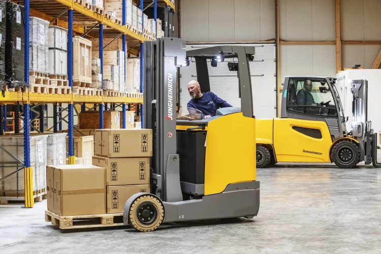 Zu sehen sind zwei Gabelstapel die geschäftig in eine Lagerhalle Ware transportieren.